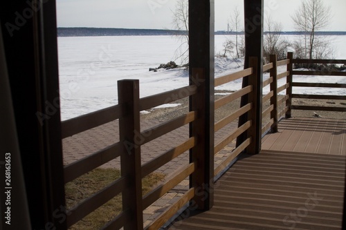 Veranda of dark brown timber. Beautiful sea view covered with ice and snow. Country rest. © olga_polyanskaya