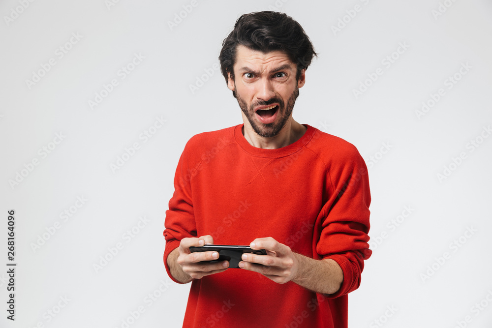 Young nervous excited man posing isolated over white wall background play games by mobile phone. Young nervous excited man posing isolated over white wall background play games by mobile phone.