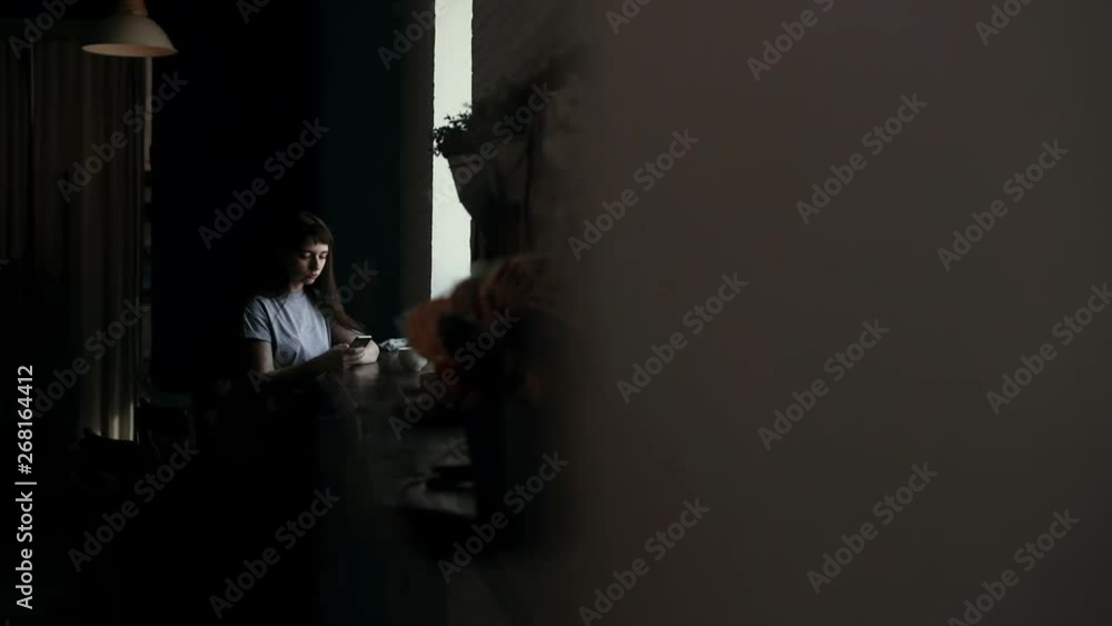 Stranger peeping at girl who drinks at cafe and typing a message on phone in slow motion. Someone is spying on young woman who drinks sitting at table in a cafe and texting. Camera moves horizontally Stranger peeping at girl who drinks at cafe and typing a message on phone in slow motion. Someone is spying on young woman who drinks sitting at table in a cafe and texting. Camera moves horizontally