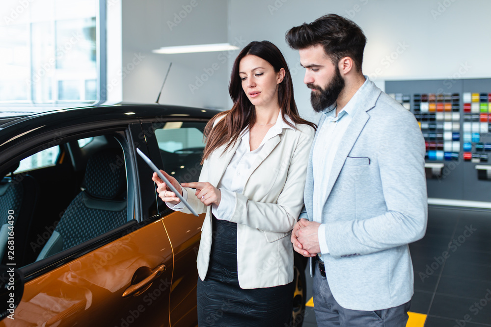 Saleswoman at the dealership showroom and young man choosing a new car for himself. Saleswoman at the dealership showroom and young man choosing a new car for himself.