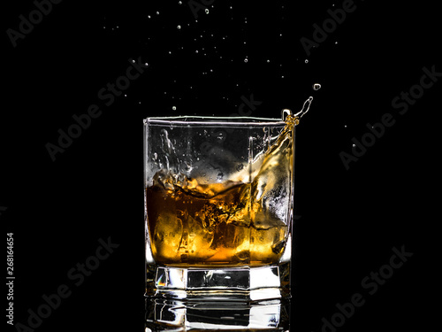 Hexagonal glass of whiskey brandy with ice and splashes from falling ice