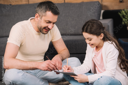 happy father drawing with cheerful daughter in living room