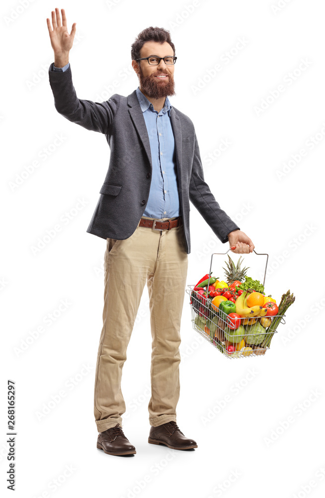 Bearded man with a shopping basket full of fruits and vegetables waving and smiling at the camera Bearded man with a shopping basket full of fruits and vegetables waving and smiling at the camera