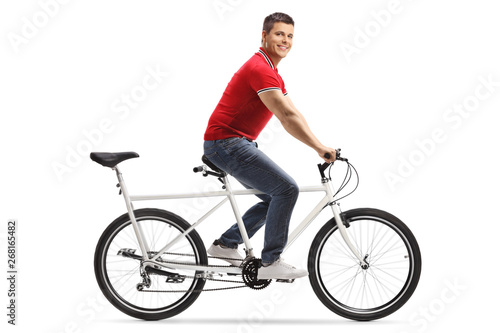 Young cheerful man riding a tandem bicycle alone and smiling at the camera