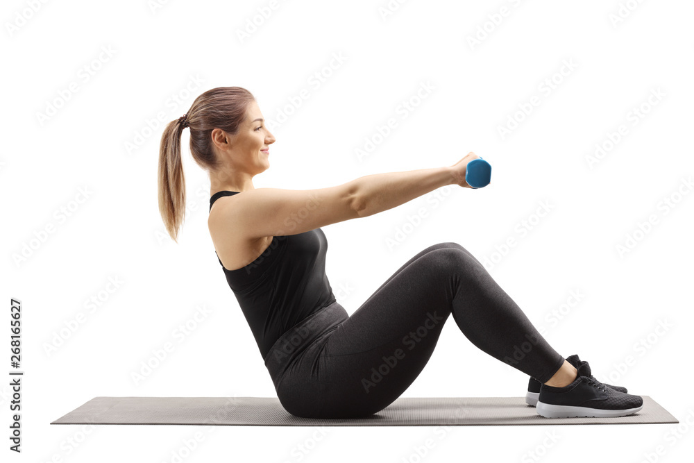 Fototapeta premium Young woman sitting on an exercising mat and working out with dumbbells