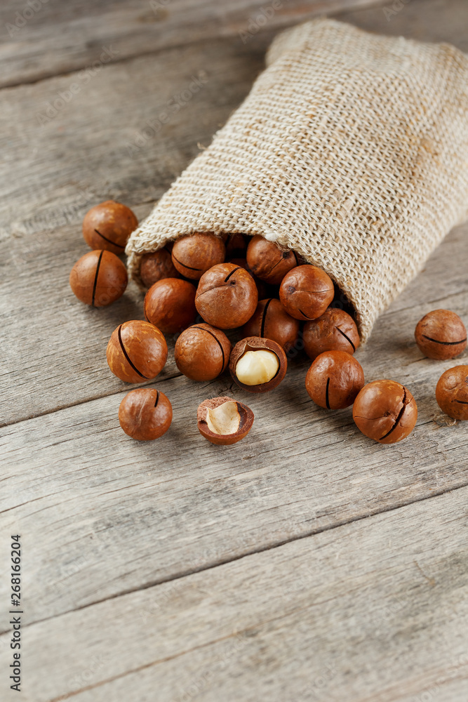 Obraz premium Macadamia nut on a wooden table in a bag, closeup, top view