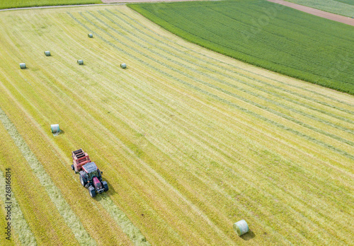 Aerial view of tractor harvesting green hay from meadow.