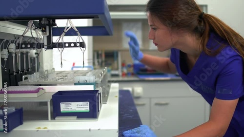 Portrait young lab assistant woman in blue uniform and rubber gloves controlling drug manufacturing in the laboratory. Conducting research in the lab. Science, profession, healthcare. Slow motion photo