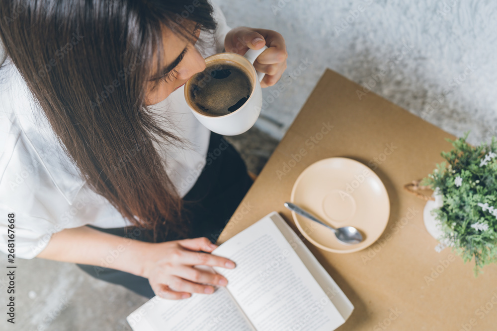 Obraz premium Close up young asian woman in white shirt reading and drinking coffee.