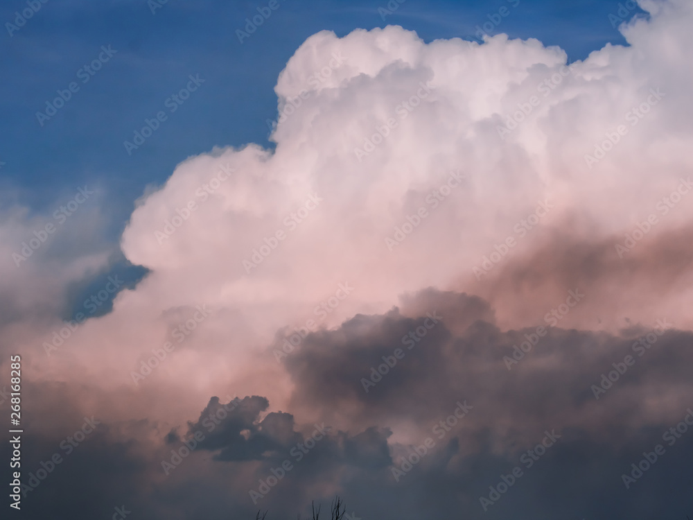 Thunder clouds, pink against the blue sky, backlit by the sun.