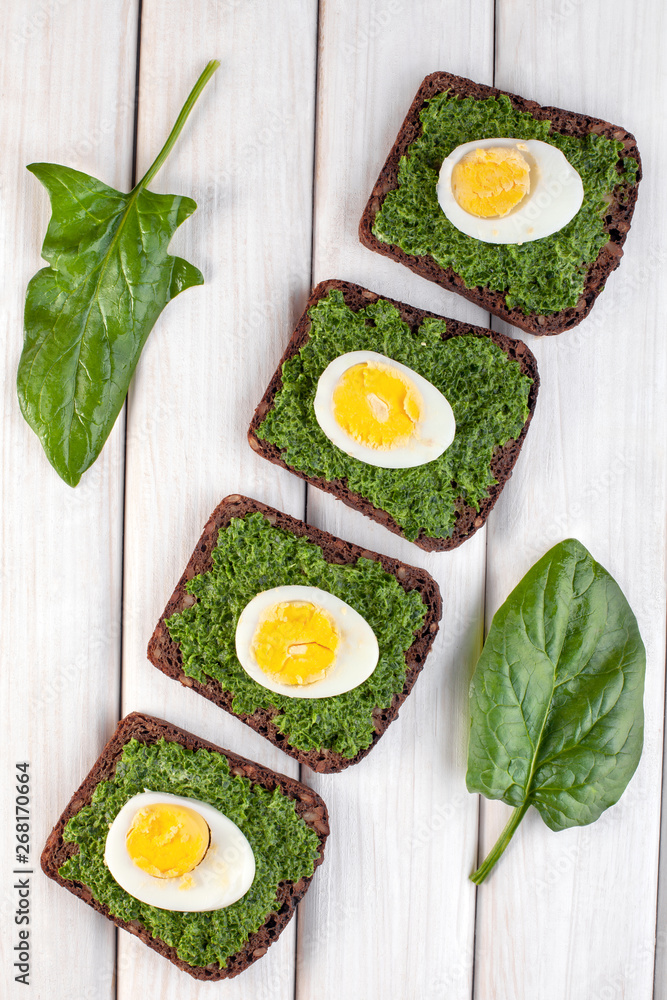 Healthy toast with mashed spinach and eggs on white wooden