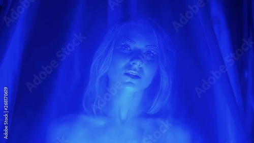 Portrait of young sexy woman with snow makeup on her eyelashes, posing under tulle erotical, blue light, winter night scene, close-up
