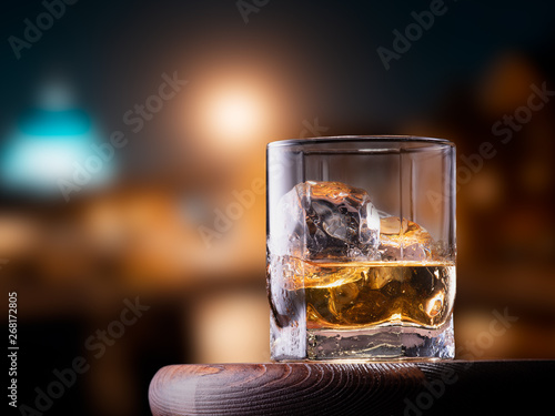 Glass of whiskey with ice cubes on the wooden table with city view background