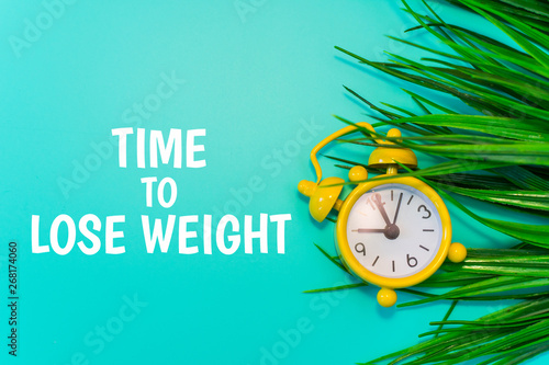 yellow alarm clock on the grass background with the inscription "Time for weight loss"
