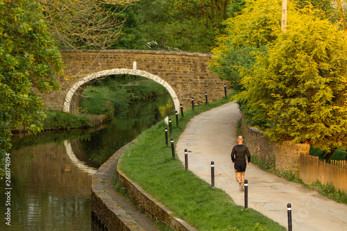 A lone runner exercises along the tow path of the Leeds and Liverpool Canal at Dowley Gap near Hirst Wood, Shipley, Yorkshire caught in the rays of the setting sun