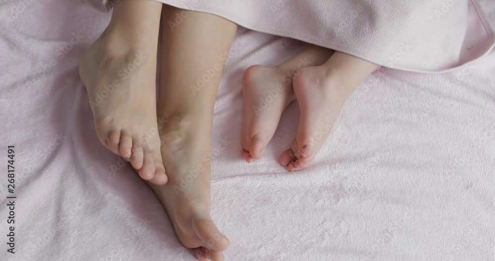 Two pairs of legs of the family in bed under the coverlet - mother and baby Two pairs of legs of the family in bed under the coverlet - mother and baby