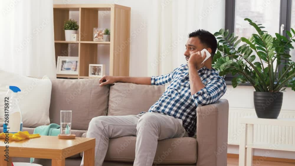 household and technology concept - indian man calling on smartphone after cleaning home household and technology concept - indian man calling on smartphone after cleaning home