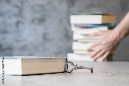 Ksiażka z kluczem na tle dłoni chwytającej sztos książek