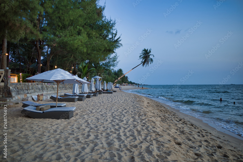 Naklejka premium Leżaki z parasolem wieczorem na ładnej długiej plaży otoczonej palmami w Phu Quoc w Wietnamie