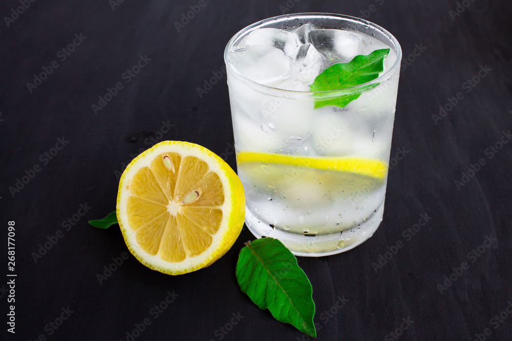 A glass of cold water with about ice, lemon and mint on a blue background A glass of cold water with about ice, lemon and mint on a blue background