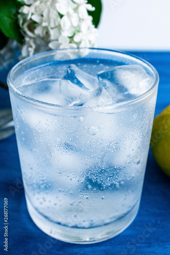  A glass of cold water with ice and lemon on a blue background