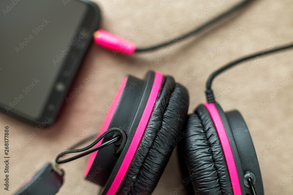 Headphone connected to cellphone isolated on light cloth flat copy space background. Modern technology, trendy entertainment, gadget design and accessories concept. Headphone connected to cellphone isolated on light cloth flat copy space background. Modern technology, trendy entertainment, gadget design and accessories concept.