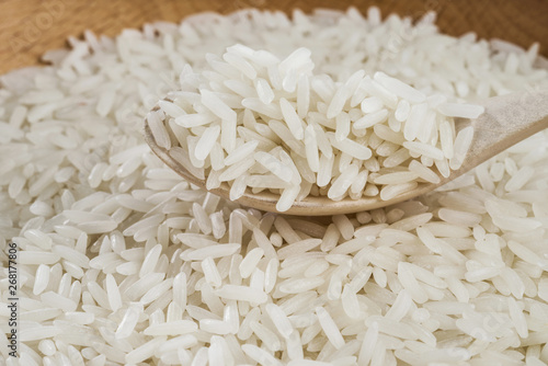 White long-grained rice on a wooden spoon on a pile of rice. Selective focus.