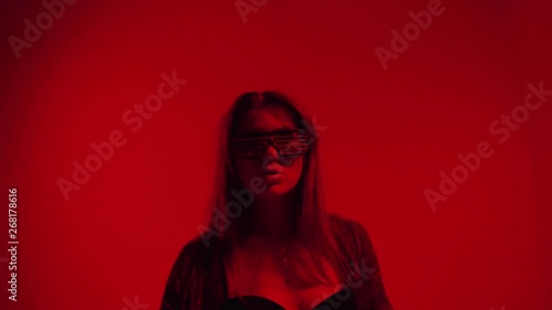 Young woman with long hair in black lingerie and led light up sunglasses dancing on red background, erotic dance in red light, moving fast, studio shot