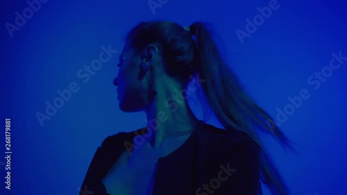 Young woman with long hair in black clothes dancing on blue background, erotic dance in ultraviolet light, moving fast, studio shot