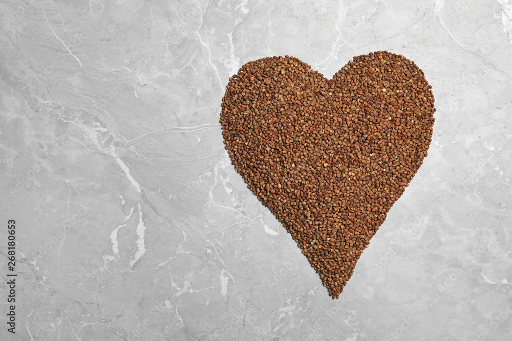 Heart made of raw buckwheat on grey background, top view. Space for text
