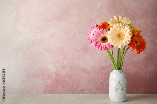 Bouquet of beautiful bright gerbera flowers in vase on marble table against color background. Space for text photo
