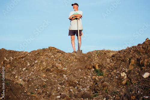 Farmer Stands On Top Of Dirt Pile With His Shover photo