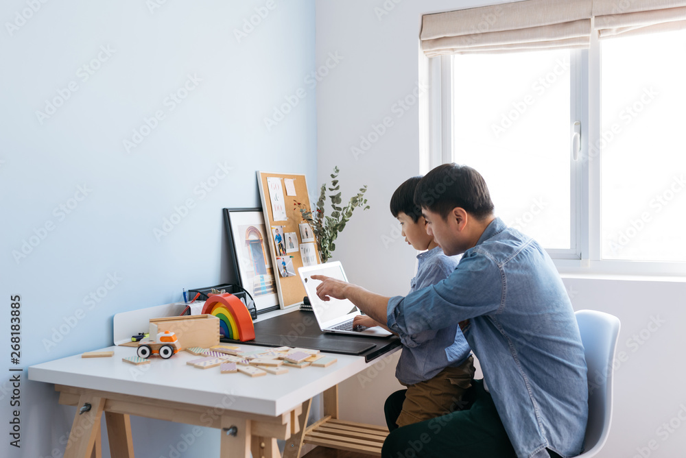 Boy sitting on father's lap behind desk in home office Boy sitting on father's lap behind desk in home office