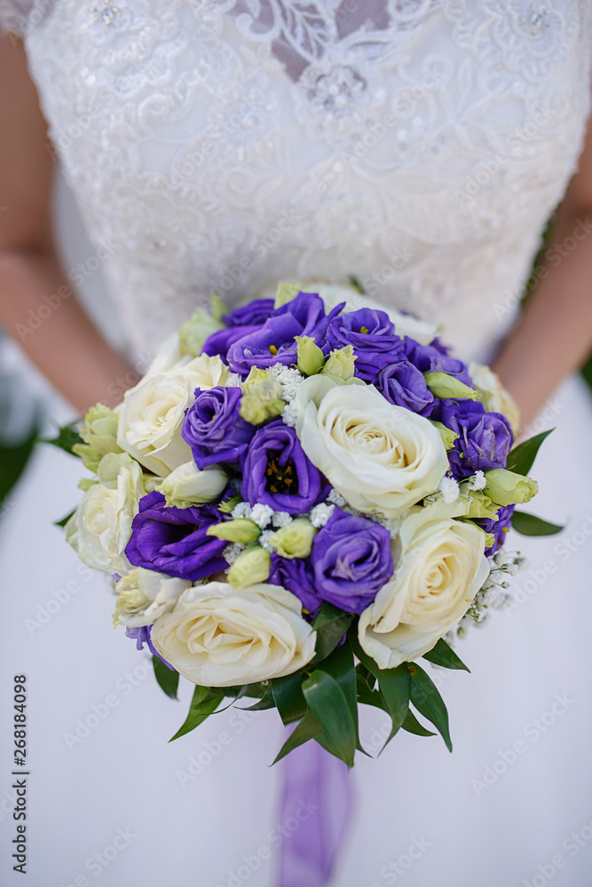 Caucasian female in beautiful lacy white dress holding a large round bouquet featuring ivory and purple roses at a wedding ceremony, traditional floral arrangement and accessory for a bride's big day Caucasian female in beautiful lacy white dress holding a large round bouquet featuring ivory and purple roses at a wedding ceremony, traditional floral arrangement and accessory for a bride's big day