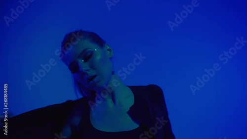 Young woman with long hair in black clothes dancing on blue background, erotic dance in ultraviolet light, moving fast sensual, studio shot