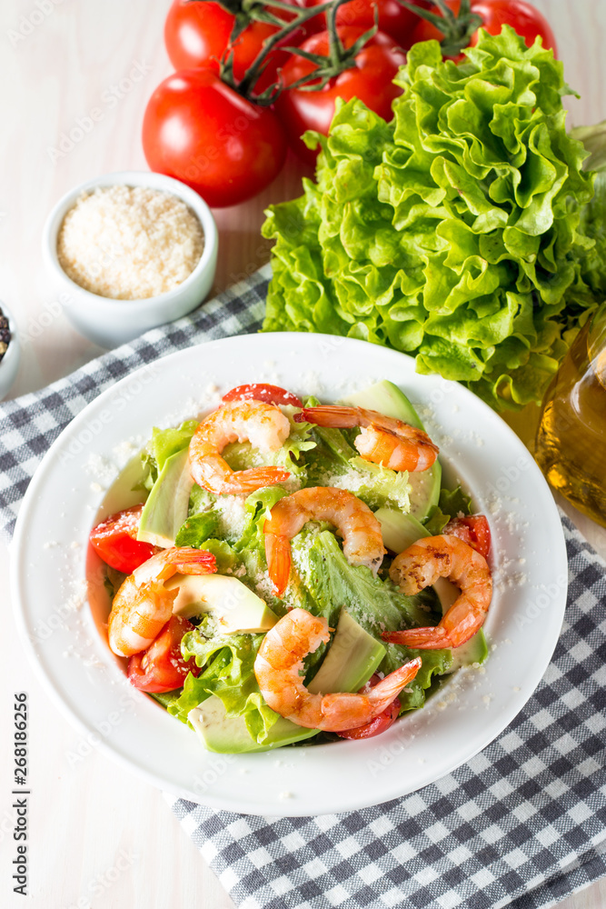 Fresh shrimp salad made of tomato, ruccola, avocado, prawns, chicken breast, arugula, crackers and spices. Caesar salad in a white, transparent bowl on wooden background Fresh shrimp salad made of tomato, ruccola, avocado, prawns, chicken breast, arugula, crackers and spices. Caesar salad in a white, transparent bowl on wooden background