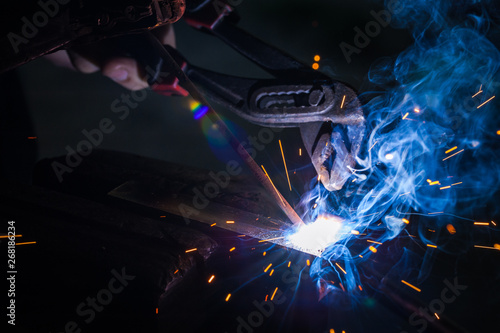 Worker with protective gloves welding metal part in workshop