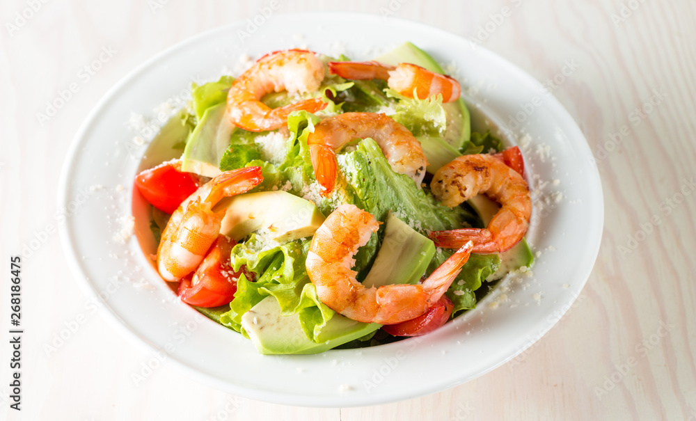 Fresh shrimp salad made of tomato, ruccola, avocado, prawns, chicken breast, arugula, crackers and spices. Caesar salad in a white, transparent bowl on wooden background Fresh shrimp salad made of tomato, ruccola, avocado, prawns, chicken breast, arugula, crackers and spices. Caesar salad in a white, transparent bowl on wooden background