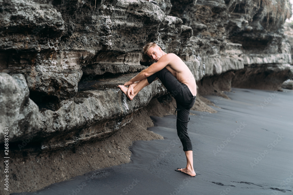 Sexy fitness male model in black pants and shirtless posing on black sandy beach. Sexy fitness male model in black pants and shirtless posing on black sandy beach.