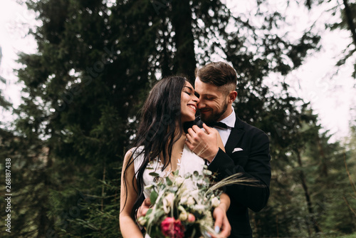 stylish couple bride and groom stand in the forest and cuddle