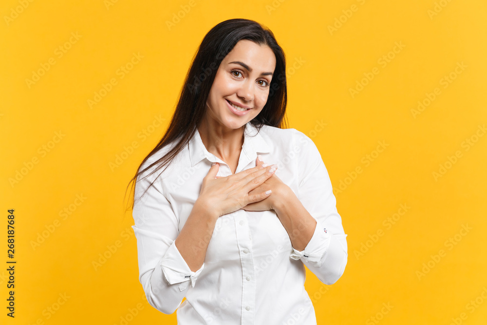 Portrait of smiling pleasant young woman in white shirt looking camera, holding hands crossed on chest, heart isolated on yellow orange wall background. People lifestyle concept. Mock up copy space. Portrait of smiling pleasant young woman in white shirt looking camera, holding hands crossed on chest, heart isolated on yellow orange wall background. People lifestyle concept. Mock up copy space.