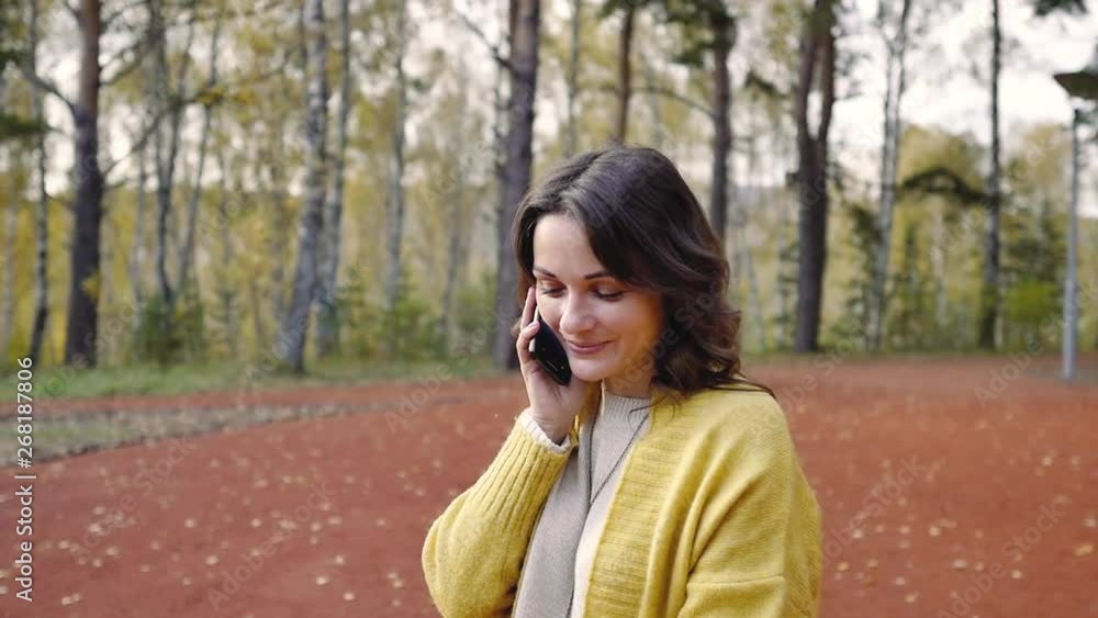 Young woman in a yellow sweater with a phone in the autumn park. woman calls by mobile phone in the park. girl makes selfie on the phone in the forest. Young woman in a yellow sweater with a phone in the autumn park. woman calls by mobile phone in the park. girl makes selfie on the phone in the forest.
