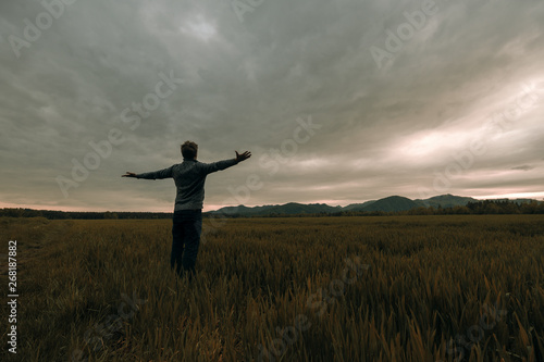 Young man standing in meadow under thunder sky