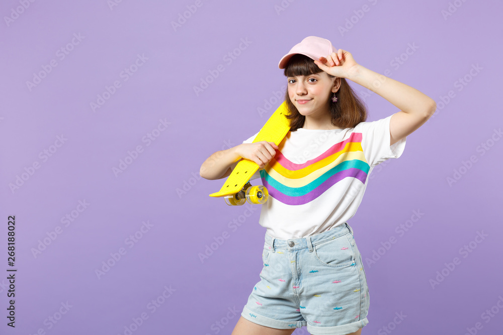 Portrait of smiling teen girl in vivid clothes looking camera, holding yellow skateboard isolated on violet pastel background in studio. People sincere emotions, lifestyle concept. Mock up copy space. Portrait of smiling teen girl in vivid clothes looking camera, holding yellow skateboard isolated on violet pastel background in studio. People sincere emotions, lifestyle concept. Mock up copy space.