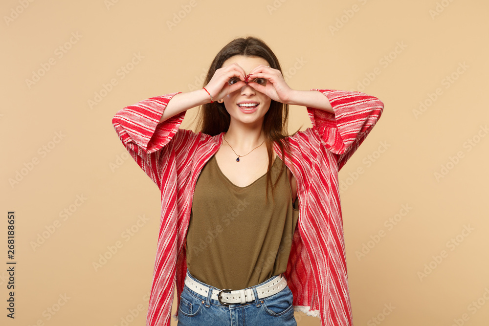 Cheerful young woman in casual clothes holding hands near eyes imitating glasses or binoculars isolated on pastel beige wall background. People sincere emotions, lifestyle concept. Mock up copy space. Cheerful young woman in casual clothes holding hands near eyes imitating glasses or binoculars isolated on pastel beige wall background. People sincere emotions, lifestyle concept. Mock up copy space.