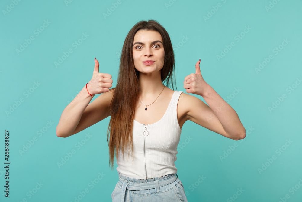 Fototapeta premium Portrait of pretty attractive young woman in light casual clothes showing thumbs up isolated on blue turquoise wall background in studio. People sincere emotions lifestyle concept. Mock up copy space.