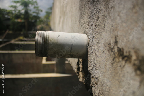 side view of an unfinished drainage pipe sticking out a grey wall