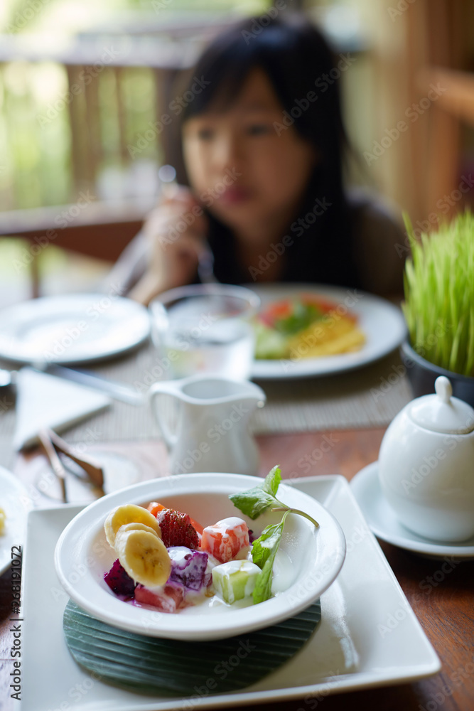 Cute Asian little girl is eating rich healthy breakfast in sunny morning Cute Asian little girl is eating rich healthy breakfast in sunny morning