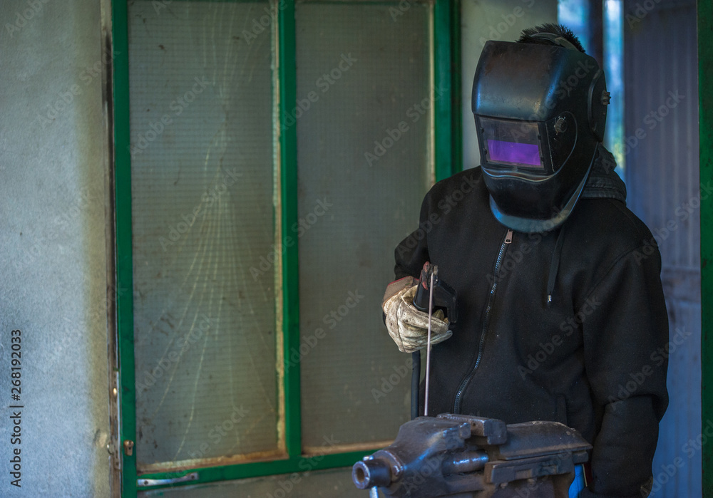Obraz premium Worker with protective gloves and protective mask welding metal part in workshop