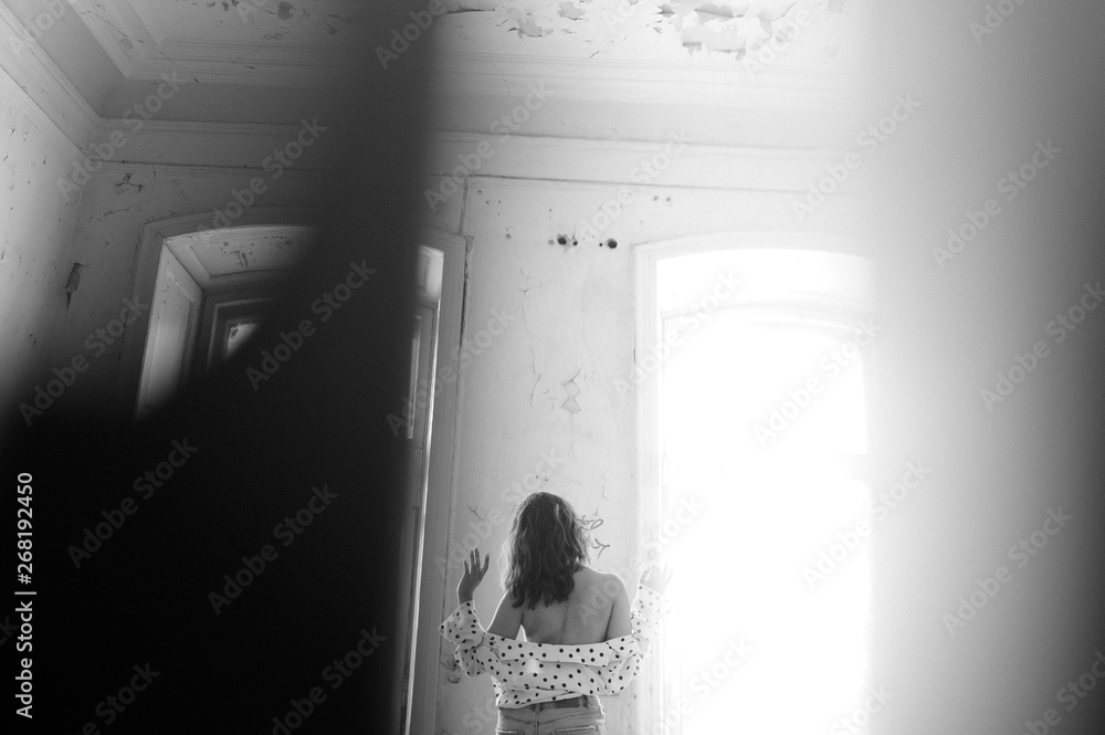 A young woman in a blouse exposes her back indoors.
